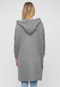 Graue Kapuzenjacke aus weichem Strickmaterial, mit einer lockeren Passform und seitlichen Schlitzierungen für Bewegungsfreiheit. Leichte Textur mit einem lässigen Design.