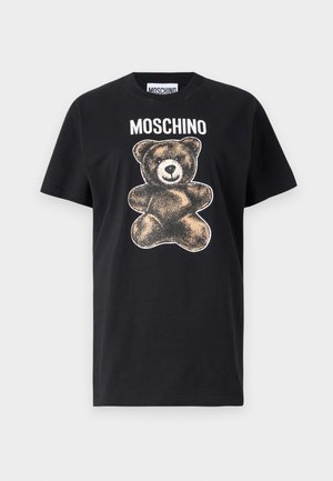 Melna kokvilnas t-kreklā ar brūnas un baltas krāsas lāča grafiku, virs lāča ir teksts "MOSCHINO". Īsas piedurknes un brīva piegriezuma.