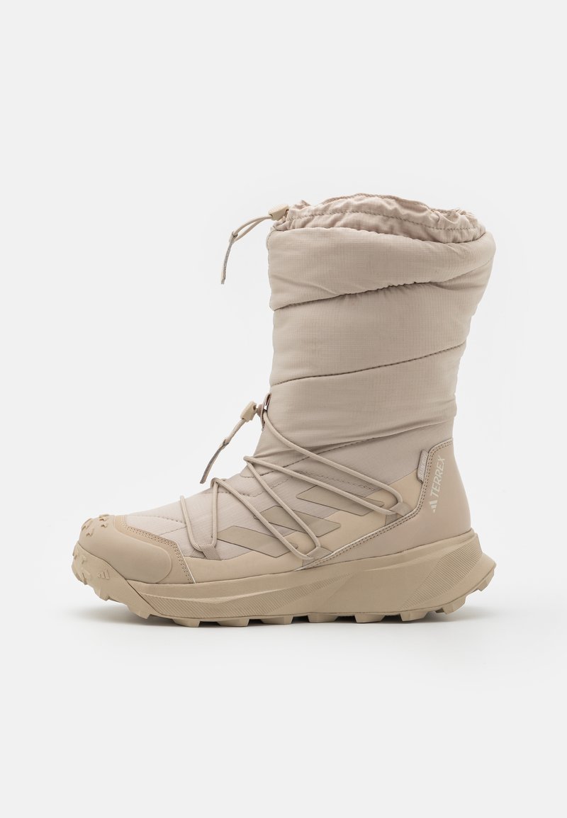 Bota aislante beige con parte superior acolchada, cuello con cordón elástico y suela de goma texturizada. Cuenta con un sistema de cordones y una puntera reforzada.