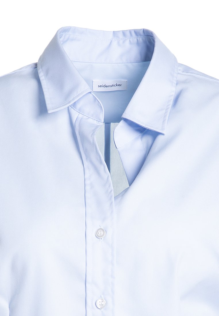 Jasnoniebieska koszula z guzikami, z wyostrzonym kołnierzykiem, gładką teksturą oraz jedną kieszonką. Metka widoczna wewnątrz kołnierza.