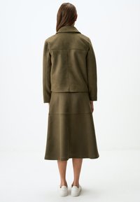 Olivgrüne Wildlederjacke mit Kragen, kombiniert mit einem passenden Midirock. Verfügt über eine Rückennaht und eine glatte Textur.