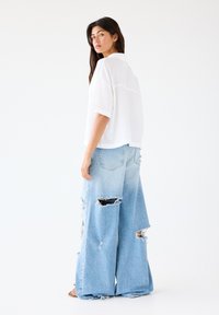 White short-sleeve blouse with a relaxed fit paired with oversized, distressed light blue denim jeans featuring large rips and frayed edges.
