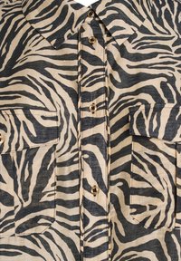 Chemise à motif zèbre en beige et noir, dotée d'un col, de deux poches poitrine, d'accents en boutons dorés et d'un tissu texturé.