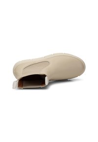 Zapato de piel beige tipo mocasín con punta redondeada, superficie texturizada y suela de goma blanca con profundas ranuras. Cuenta con un lazo en la parte trasera para facilitar el calzado.