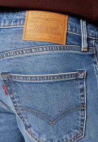 Ljust blå denimjeans med en läderpatch märkt "Levi Strauss & Co." och synlig sömnad; har en bakficka med röd tab och emblem.