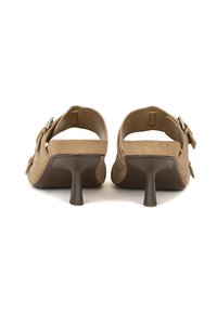 Sandali con tacco in suede beige con tacco curvo marrone, apertura sul retro e dettagli decorativi a forma di fibbia ai lati. Sole piatto sotto il tacco.