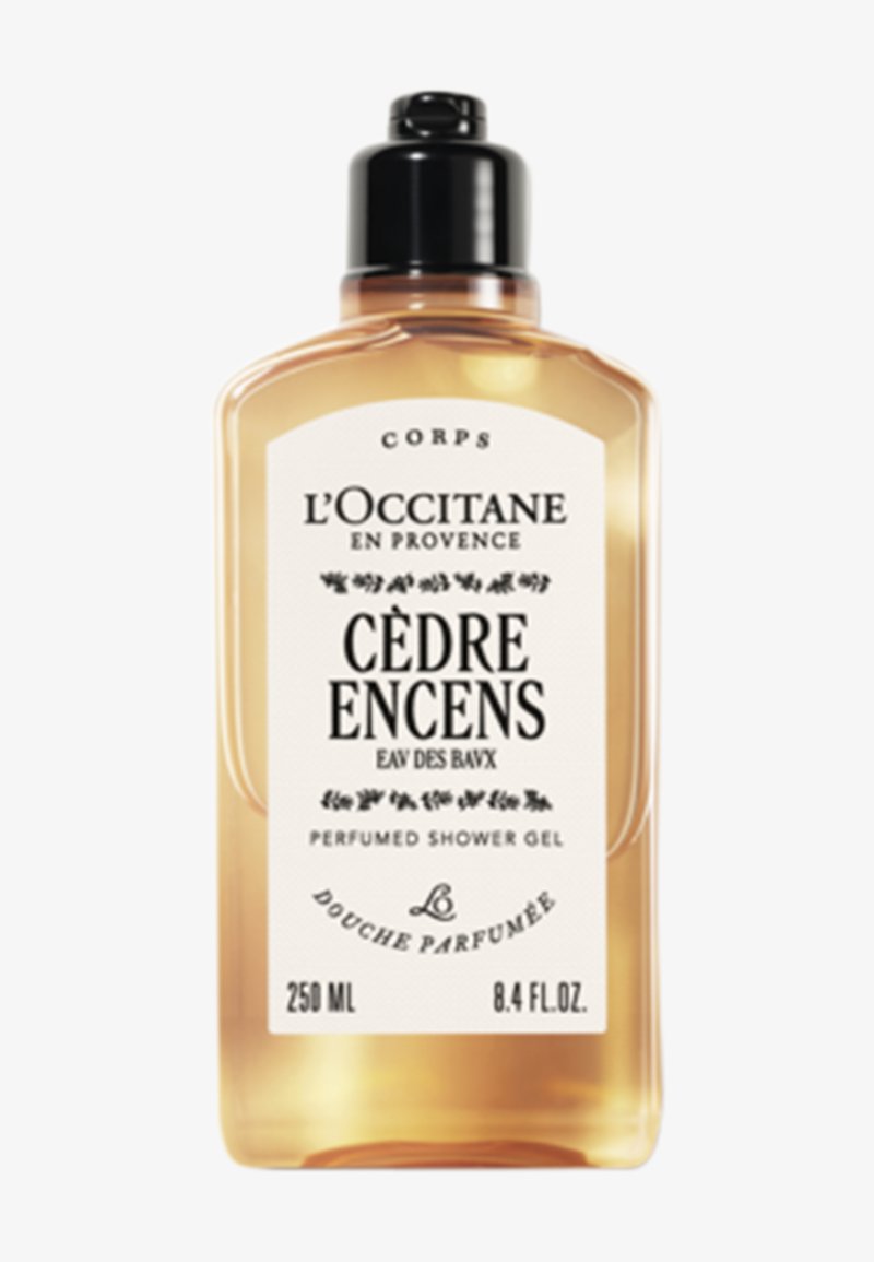 Genomskinlig flaska med parfymduschgel, gyllene vätska, svart pumpkork, vit etikett med logotyp och text, 250 ml kapacitet.