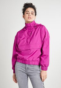 Rosa, lettvekts hettejakke som er vindtett, med elastiske kanter og hem. Den har en kenguru-lomme og en halv glidelås foran.