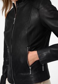 Svart läderjacka med hög krage, dragkedja framtill och sidofickor. Har slanka linjer och silverfärgad dragkedja.