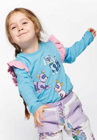 Camicia a maniche lunghe blu con accenti a ruches rosa, caratterizzata da cani robotici dei cartoni animati. Abbinata a pantaloni viola chiaro stampati con disegni simili.