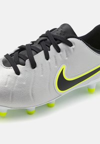 Chaussure de football Nike avec une tige en cuir argenté et des accents noirs, un logo avec des détails jaunes et des crampons verts vifs sur la semelle.