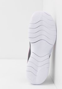 Zool van een schoen met wit rubberen materiaal, een gestructureerd oppervlak en golvende groeven. Heeft een zwart bovenstuk met roze accenten aan de zijkanten.