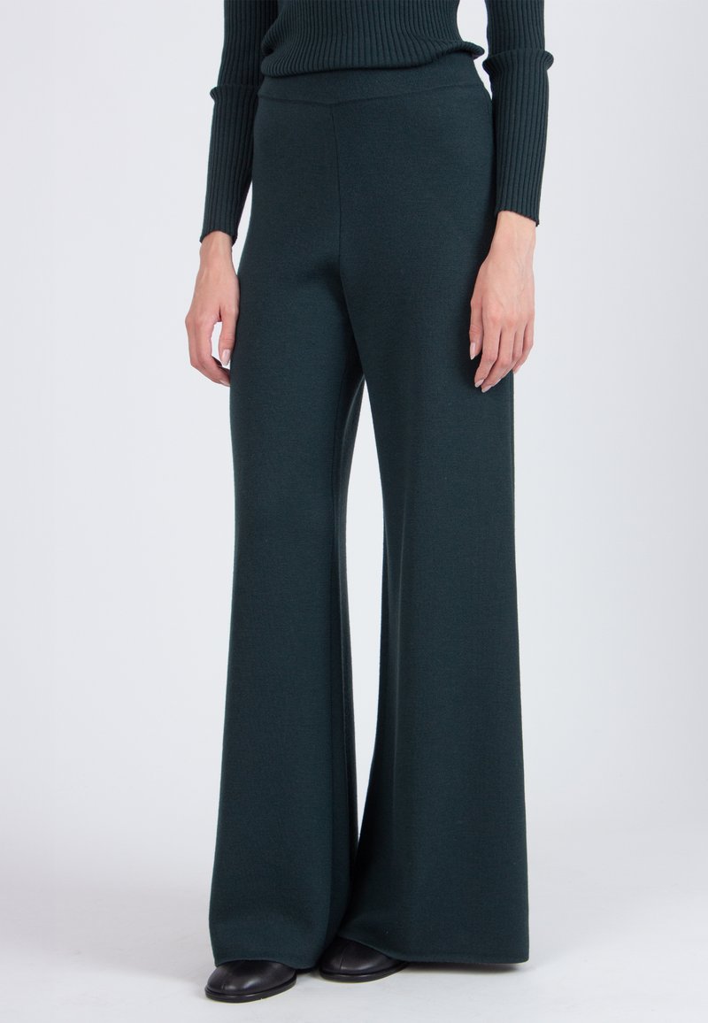 Wide-leg pants made of dark green fabric with a smooth texture. Features a high waistband and pairs with black footwear.