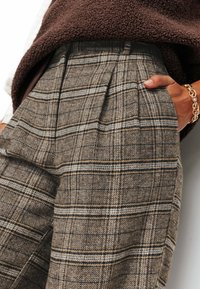 Pantalons à carreaux bruns avec un tissu texturé, des plis, des poches latérales et des accents en bleu clair et noir.