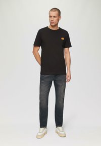 Czarny bawełniany t-shirt z pomarańczowym wzorem dyni na lewej piersi, w połączeniu z przetartymi ciemnymi dżinsami i białymi trampkami.