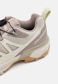 Scarpa sportiva con tomaia in rete grigia chiara testurizzata e rosa morbido, suola in gomma e distintivo cordino di traino. Presenta un design minimalista e lacci regolabili.