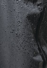 Schwarzer wasserdichter Stoff mit sichtbaren Wassertropfen, der eine glatte Textur und einen subtilen Glanz zeigt, mit einem Reißverschlussdetail auf einer Seite.