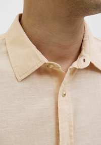 Licht perzikkleurig linnen overhemd met een button-down kraag, voorzien van een enkele knoopsluiting bij de hals, een gladde textuur en zichtbare stiksels.