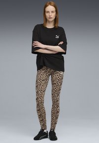 Zwarte oversized t-shirt met een Puma-logo, gecombineerd met legging met luipaardprint en zwarte sneakers, met een gladde textuur en een rekbare pasvorm.