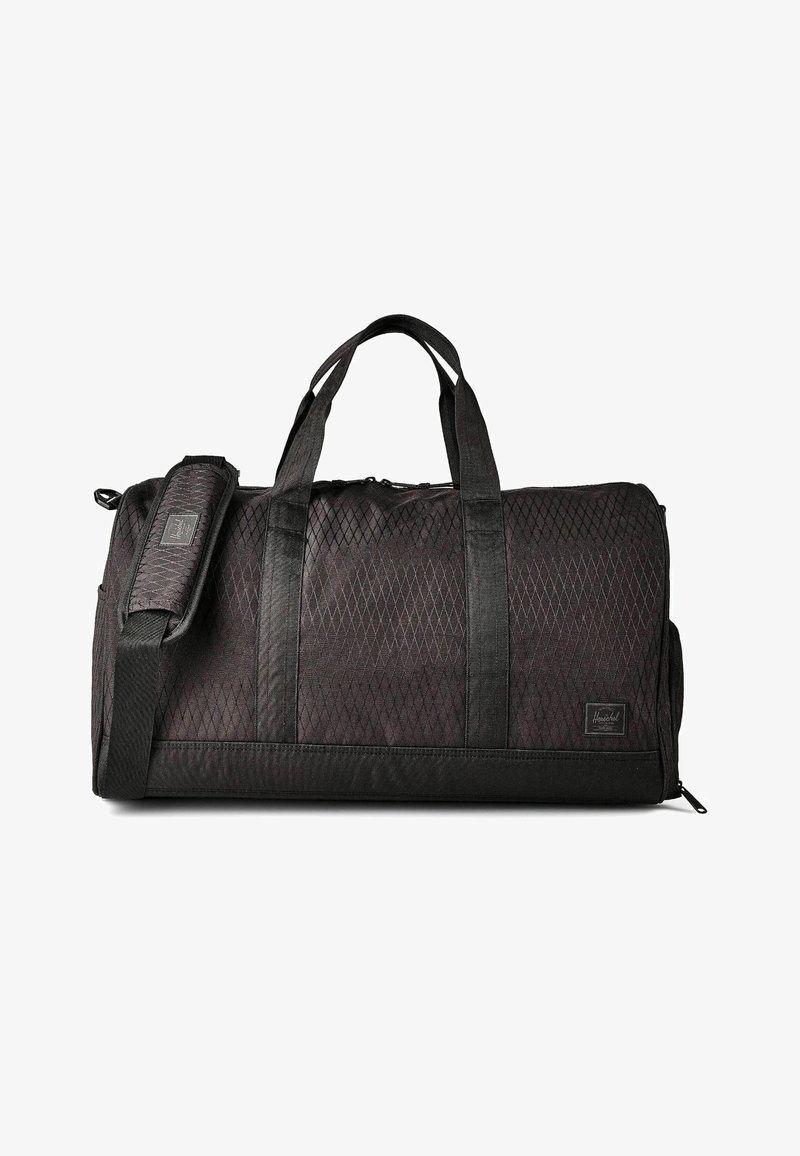 Sac de sport noir en tissu à motif losange, avec deux poignées de transport, une bandoulière réglable, et une petite étiquette rectangulaire de marque sur le devant.