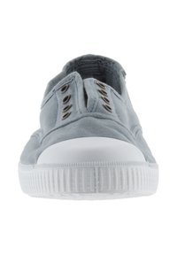 Grå lærred slip-on sko med en hvid gummisål, der har tre metaløjer og et tekstureret mønster på sålen for greb.