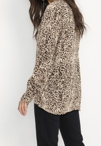 Leopard print long-sleeve blouse in beige and brown, made of lightweight fabric, feature loose fit and gathered shoulders. Black pants visible below.
