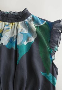Dark blue sheer blouse with large white and green floral print and ruffled neckline and cap sleeves on a white background.