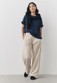 Navy blue t-shirt with rolled sleeves, paired with cream jogger pants and black sneakers. The joggers feature an elastic waistband.