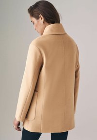 Beige Wolle-Mischung Mantel mit ausgeschnittenem Kragen, einer einzelnen Rückennaht und Seitentaschen, die eine glatte Textur und eine taillierte Passform aufweist.