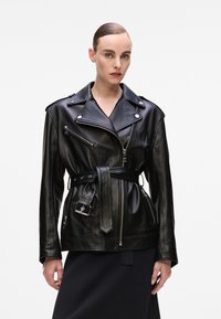 Black leather motorcycle jacket with a belted waist, zip pockets, and silver hardware accents. Features a notched lapel and tailored fit.