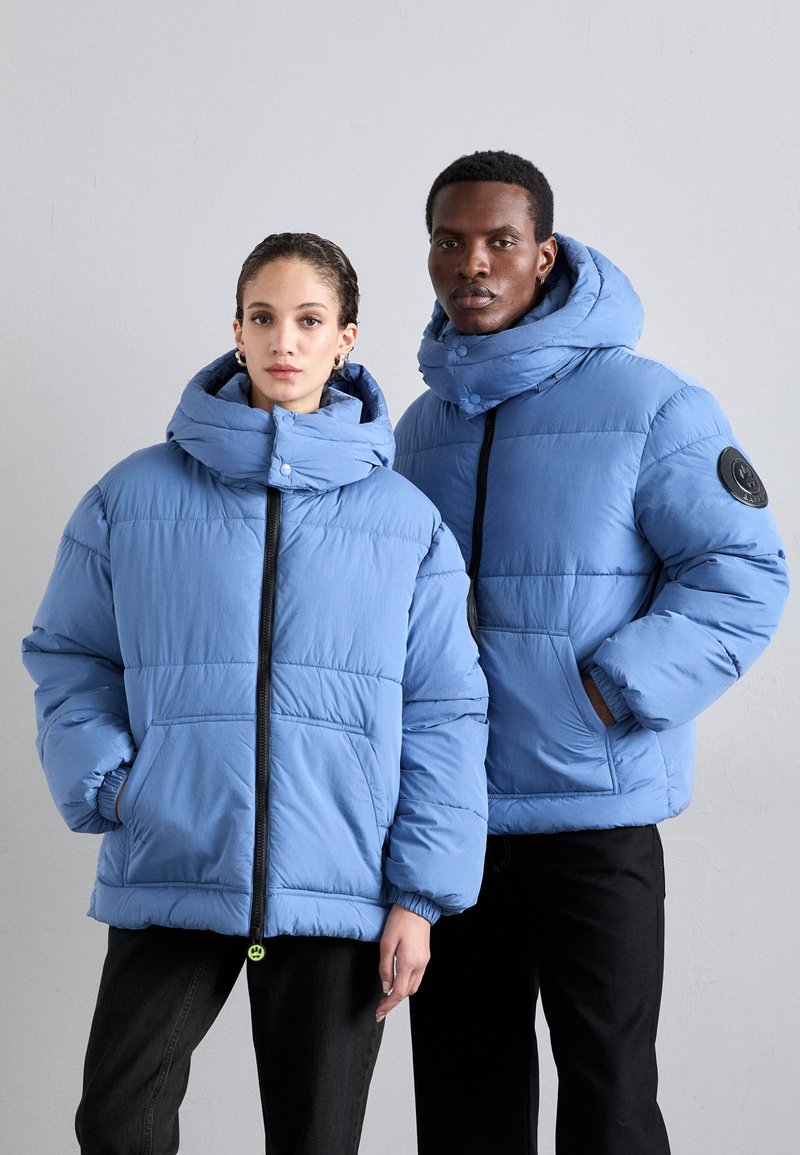 Hellblaue Pufferjacken mit großen Kapuzen, Fronttaschen und kontrastierenden schwarzen Reißverschlüssen. Beide Jacken haben eine gesteppten Textur und Akzente.