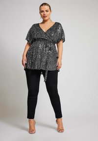 Top nero con paillettes, scollato a V e maniche corte, strizzato in vita con un nastro. Abbinato a jeans skinny neri e scarpe con tacco a strappo argentate.