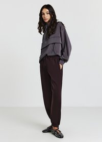 Sweatshirt gris en couches avec des manches amples, associé à un jogging bordeaux foncé. Des chaussures noires à enfiler présentent un motif circulaire. Coupe simple et décontractée.