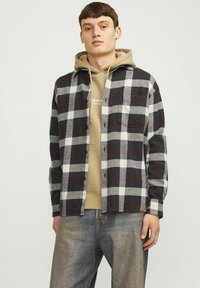 Skakettet flannel skjorte i mørk navy, hvid og grå, med en brystlomme, knaplukning og båret over en beige hoodie.