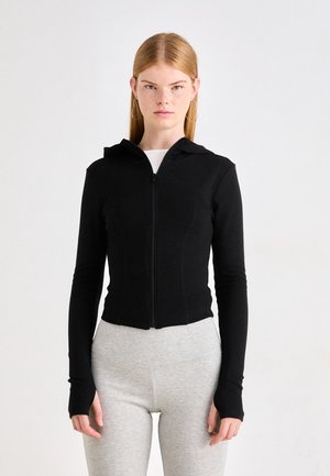 Sweatshirt preto com fecho, de design ajustado, mangas longas e capuz. O tecido parece liso e elástico, complementado por orifícios para os polegares nas mangas.