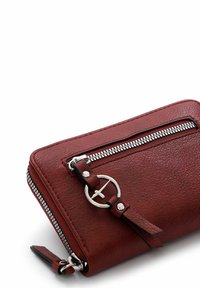 Red leather wallet with textured finish, silver zipper, and an accent strap with a circular metal hardware detail. Rounded edges.