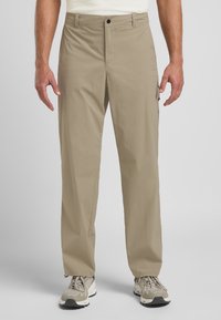 Pantaloni cargo beige con taglio dritto, realizzati in tessuto leggero. Presentano tasche laterali e chiusura con zip. Indossati con sneaker grigie e beige.