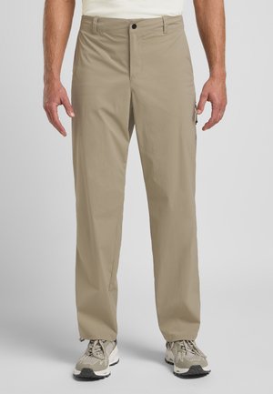 Pantalons cargo beiges à coupe droite, fabriqués en tissu léger. Comprend des poches latérales et une fermeture éclair. Portés avec des baskets grises et beiges.