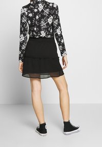 Svart blommig blus med lång ärm och vita blommor, tillsammans med en svart lagerkjol och svarta högskoor. Mjuk och avslappnad design.