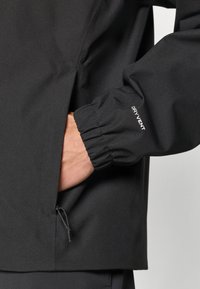 Μαύρο αδιάβροχο μπουφάν με ελαστικά μανίκια, πλαϊνή τσέπη με κορδόνι και τη σήμανση «DRY VENT» στο μανί κι.