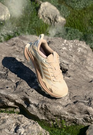 Beige Sport-Schuh mit strukturiertem Obermaterial, Gummisohle und Mesh-Details. Verfügt über dezente Markenkennzeichnung und einen gepolsterten Kragen für zusätzlichen Komfort.