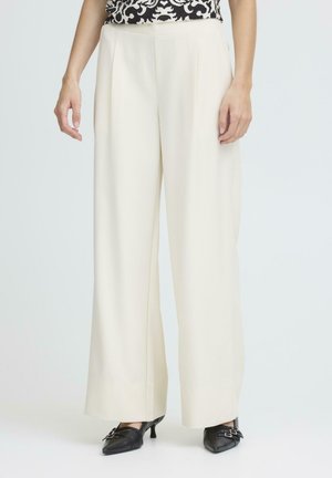 Pantalones de pierna ancha color crema con una textura suave, con plisados frontales y cintura alta, combinados con zapatos de tacón negros con hebillas.