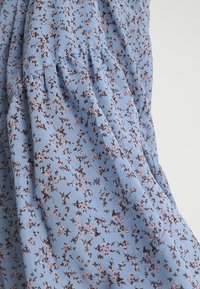 Tissu à imprimé floral bleu clair avec de petites fleurs brunes et roses. Présente des détails froncés pour ajouter de la texture. Matériau lisse et léger.