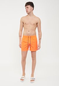 Pantaloni da bagno neon arancioni realizzati in tessuto ad asciugatura rapida, con vita regolabile e dettagli in bianco e nero.