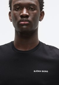 Μαύρο κοντομάνικο μπλουζάκι με στρογγυλή λαιμόκοψη, με λευκό λογότυπο "BJÖRN BORG" στο αριστερό μέρος του στήθους. Ομαλή υφή από βαμβάκι.