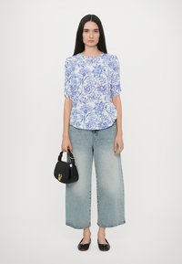 Top blu con motivo floreale e maniche a sbuffo, abbinato a jeans a gamba larga blu chiaro, borsa nera e ballerine nere.