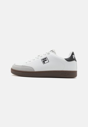 White sneakers with gray and black accents, featuring a smooth leather upper, round toe, and textured brown rubber sole. Black logo detail on the side.