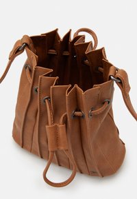 Borsa a secchiello in pelle marrone con chiusura a coulisse, cuciture visibili e tracolla regolabile su sfondo bianco.