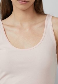 Lichtroze tanktop met een ronde halslijn en dunne bandjes, gemaakt van glad, rekbaar materiaal. Platte naaddetails zichtbaar rond de randen.