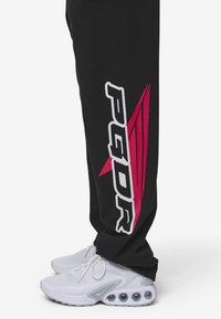 Svart joggingsbyxor med vit och rosa "PQDR"-logotyp och designelement. I kombination med vita mönstrade sneakers med luftkuddar.